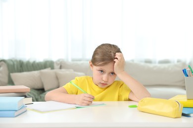 Photo of Tired little girl doing homework at table indoors