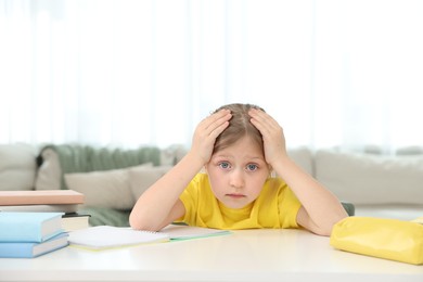 Photo of Tired little girl doing homework at table indoors