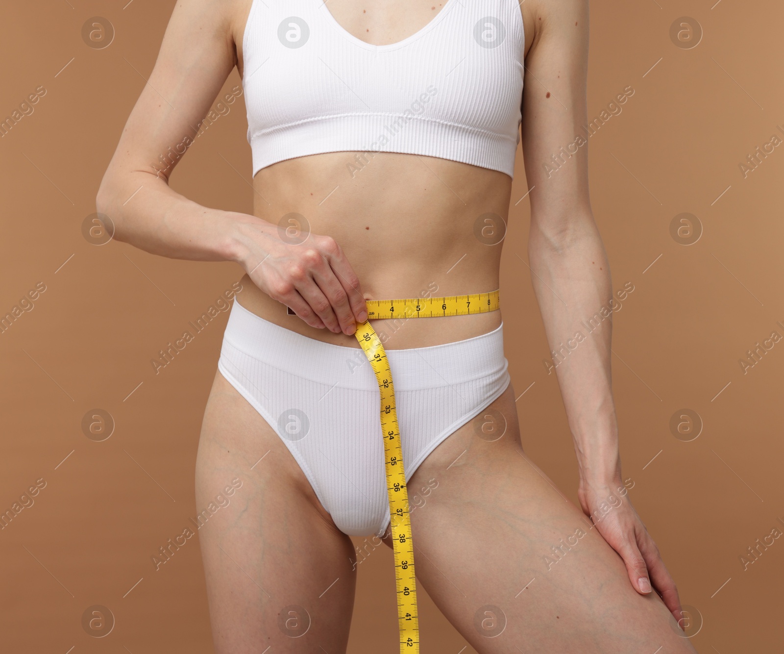 Woman with slim body and measuring tape on beige background, closeup Photo of Woman with slim body and measuring tape on beige background, closeup