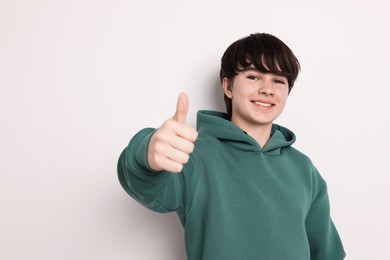 Photo of Portrait of teenage boy showing thumbs up on white background, space for text