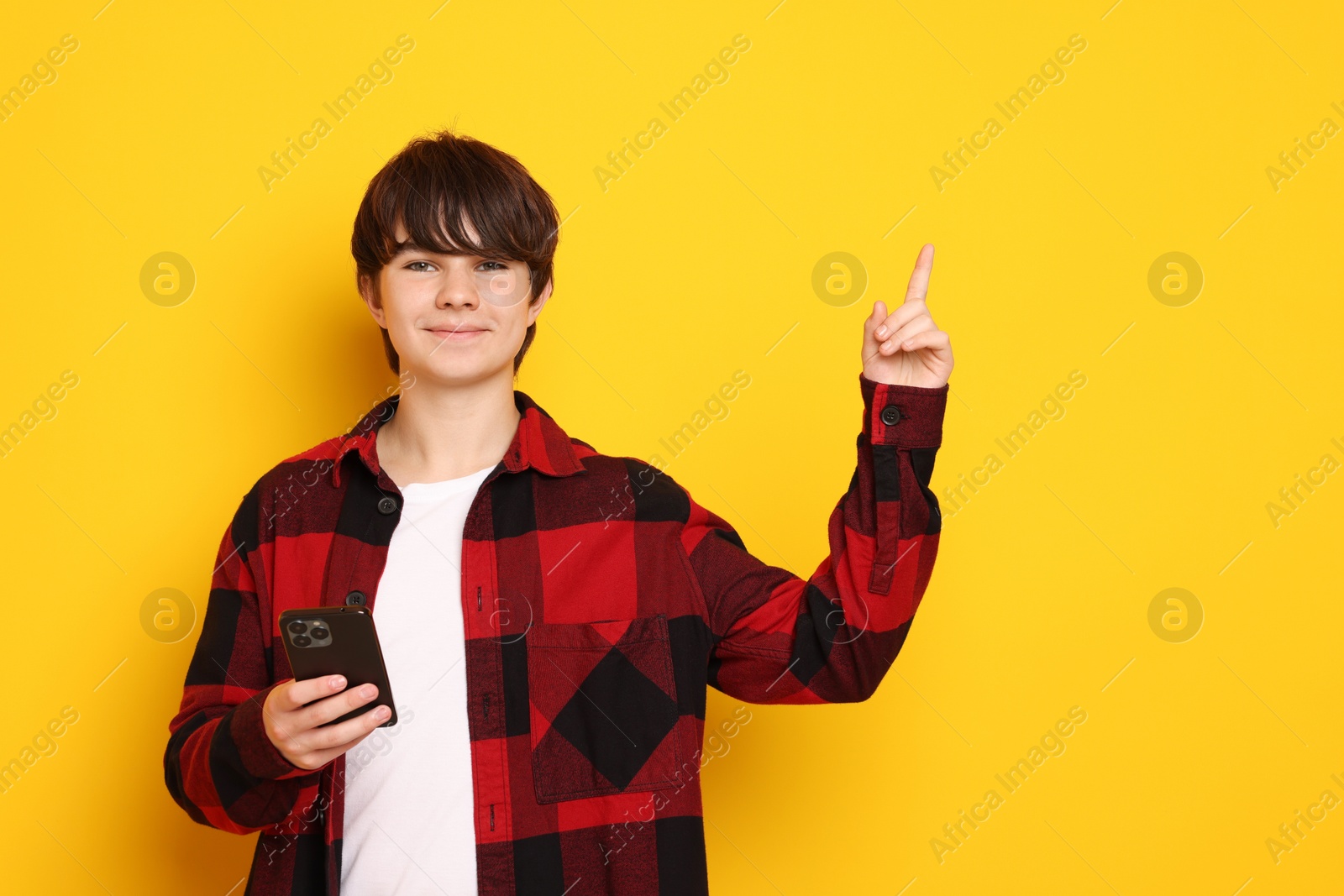 Teenage boy with smartphone on orange background, space for text Photo of Teenage boy with smartphone on orange background, space for text