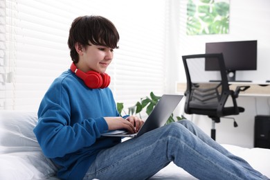 Photo of Teenage boy with headphones and laptop on bed at home
