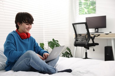 Photo of Teenage boy with headphones and laptop on bed at home, space for text