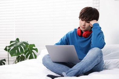 Photo of Teenage boy with headphones and laptop on bed at home, space for text