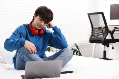 Photo of Teenage boy with headphones and laptop on bed at home, space for text