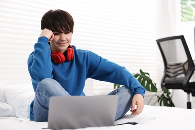 Photo of Teenage boy with headphones and laptop on bed at home