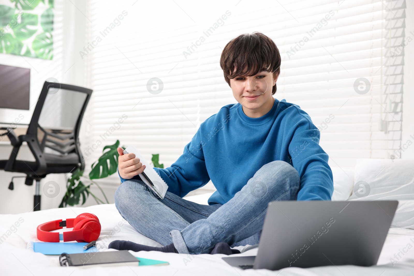 Teenage boy doing homework on bed indoors Photo of Teenage boy doing homework on bed indoors