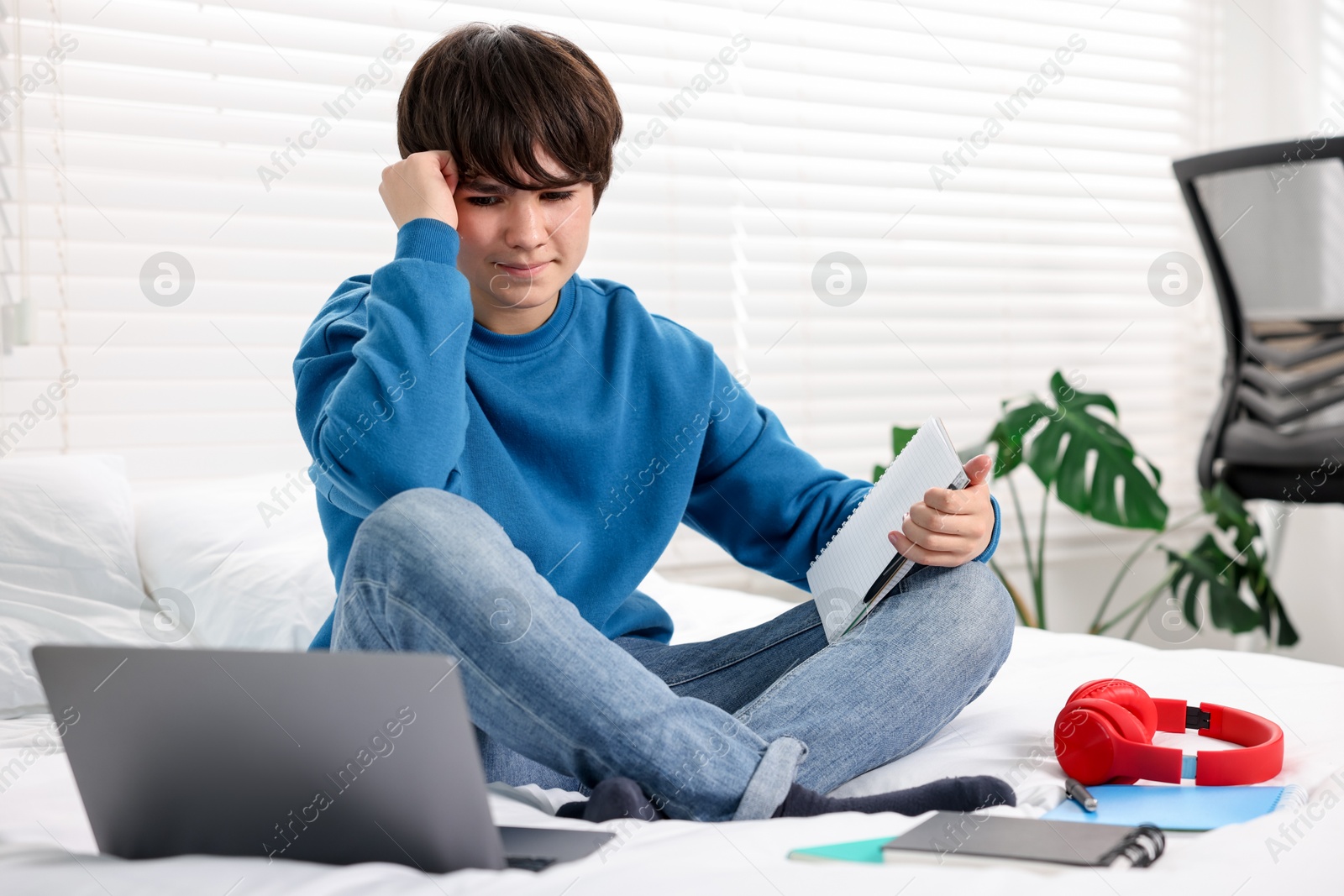 Photo of Teenage boy doing homework on bed indoors