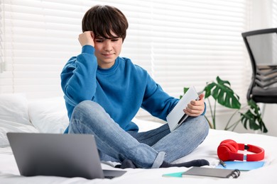 Photo of Teenage boy doing homework on bed indoors