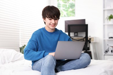 Photo of Teenage boy with laptop on bed at home