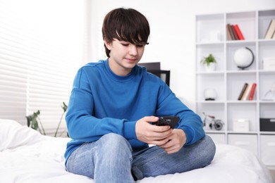 Photo of Teenage boy with smartphone on bed at home