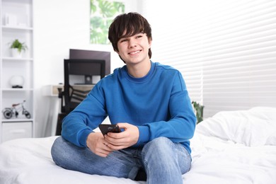 Photo of Teenage boy with smartphone on bed at home