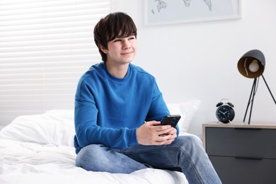 Photo of Teenage boy with smartphone on bed at home
