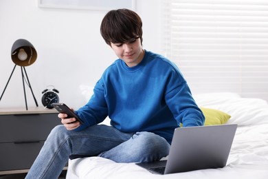 Photo of Teenage boy with smartphone and laptop on bed at home