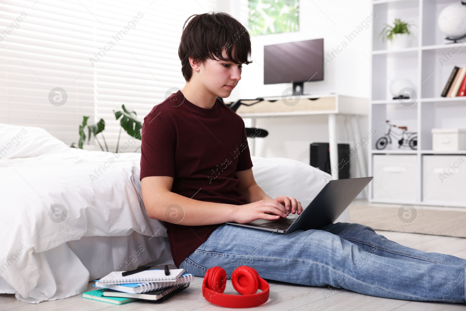 Teenage boy doing homework near bed indoors Photo of Teenage boy doing homework near bed indoors