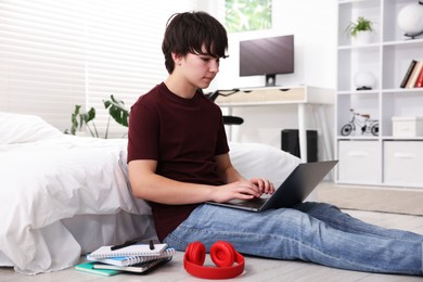 Photo of Teenage boy doing homework near bed indoors