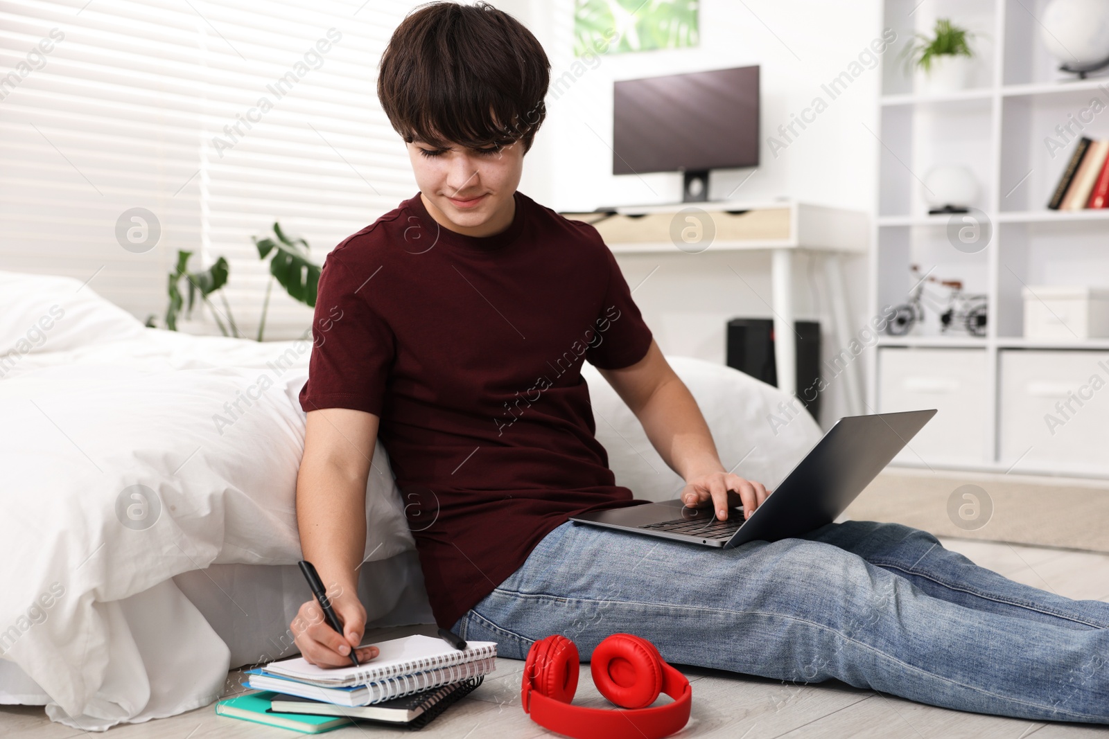 Teenage boy doing homework near bed indoors Photo of Teenage boy doing homework near bed indoors