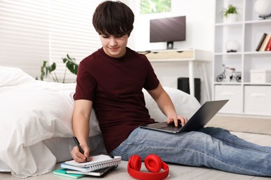 Photo of Teenage boy doing homework near bed indoors