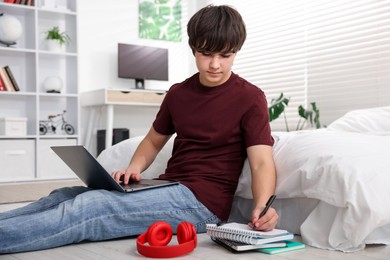 Photo of Teenage boy doing homework near bed indoors