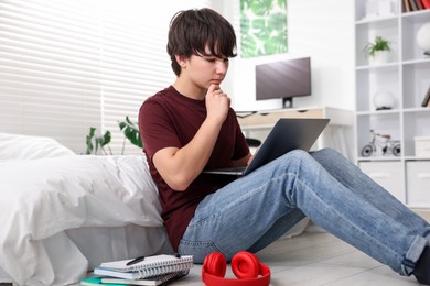 Photo of Teenage boy doing homework near bed indoors