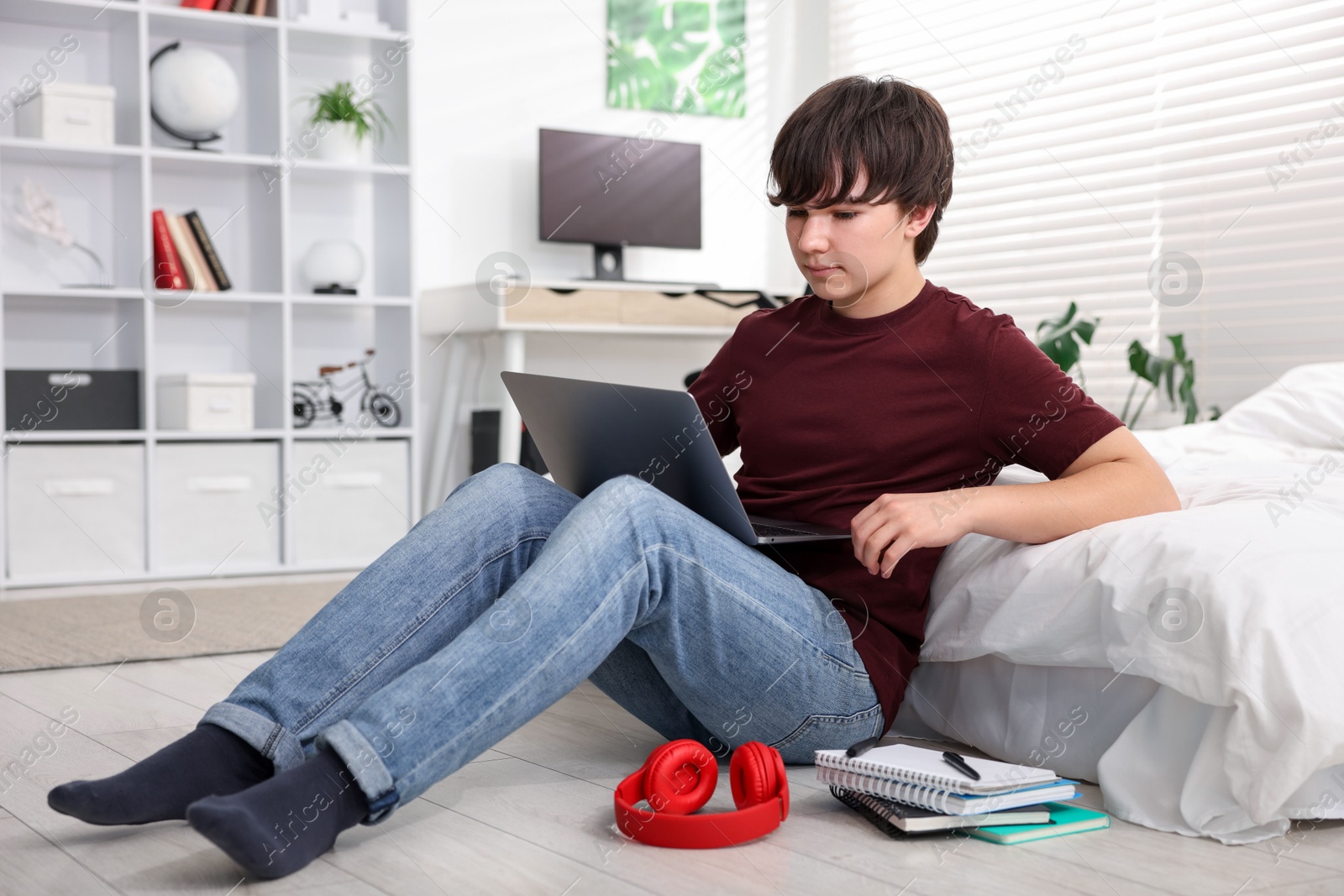 Teenage boy doing homework near bed indoors Photo of Teenage boy doing homework near bed indoors
