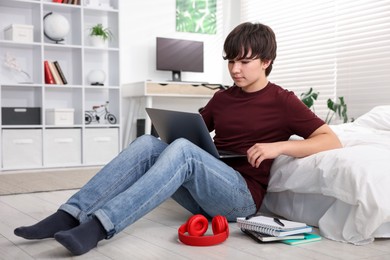 Photo of Teenage boy doing homework near bed indoors
