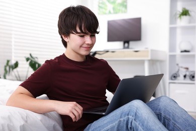 Photo of Teenage boy using laptop near bed at home