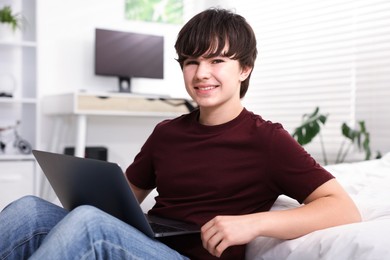 Photo of Teenage boy using laptop near bed at home