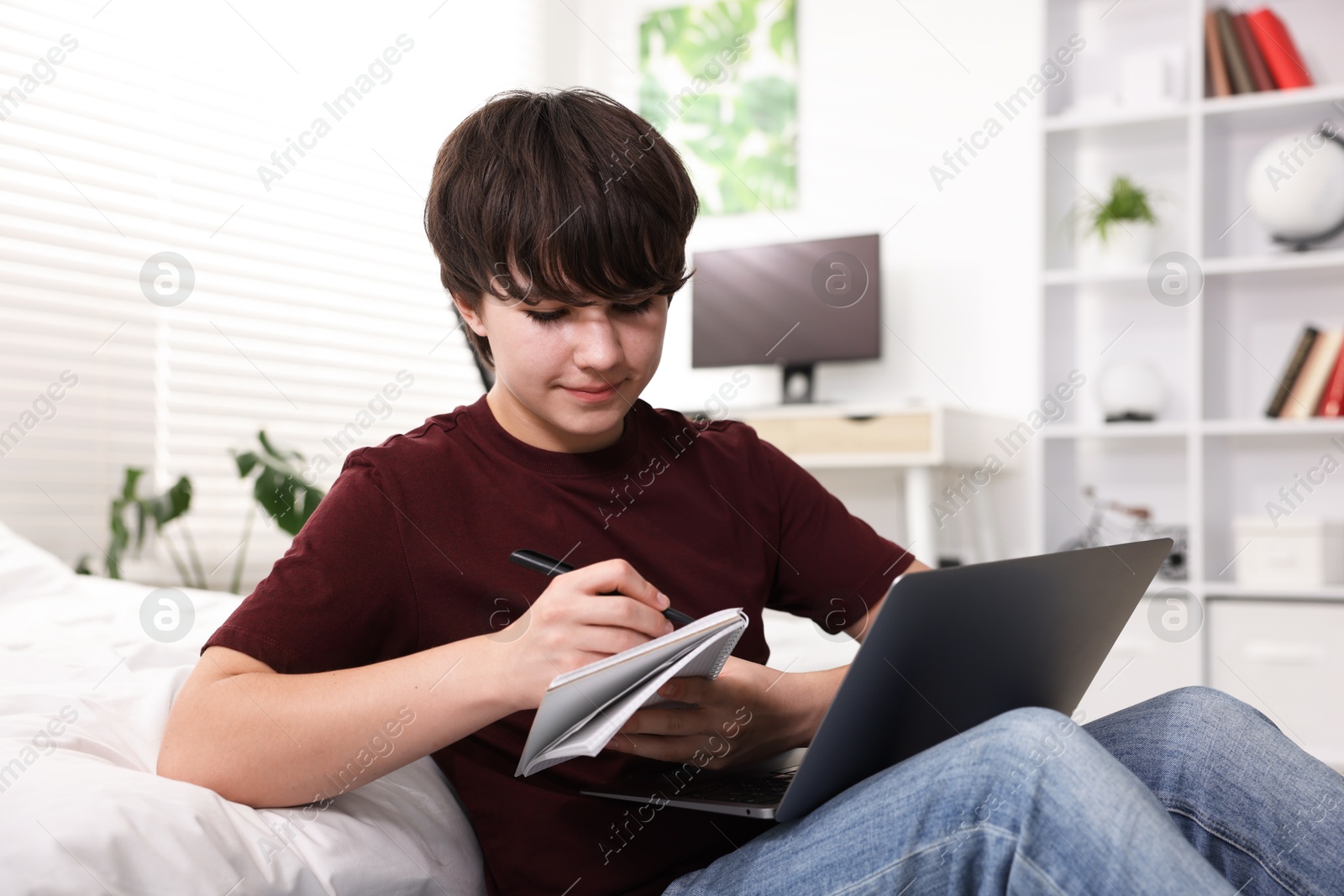 Teenage boy doing homework near bed indoors Photo of Teenage boy doing homework near bed indoors