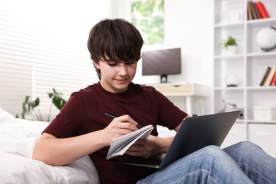 Photo of Teenage boy doing homework near bed indoors