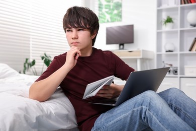 Photo of Teenage boy doing homework near bed indoors