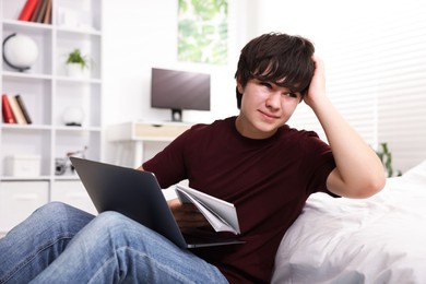 Photo of Teenage boy doing homework near bed indoors