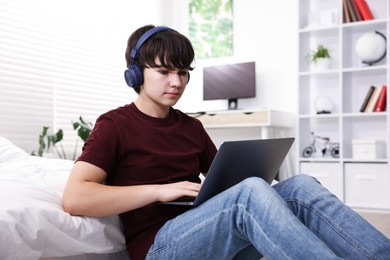 Photo of Teenage boy in headphones using laptop at home