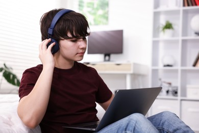 Photo of Teenage boy in headphones using laptop at home