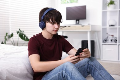 Photo of Teenage boy in headphones using smartphone at home