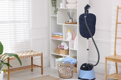 Photo of Modern upright steamer and basket with clean laundry indoors