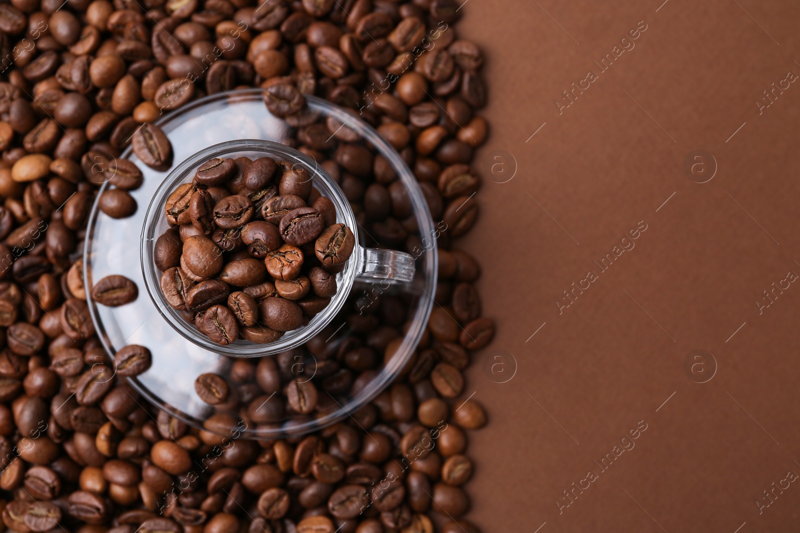 Aromatic coffee beans, cup and saucer on brown background, flat lay. Space for text Photo of Aromatic coffee beans, cup and saucer on brown background, flat lay. Space for text