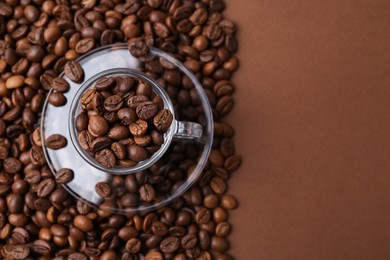 Photo of Aromatic coffee beans, cup and saucer on brown background, flat lay. Space for text