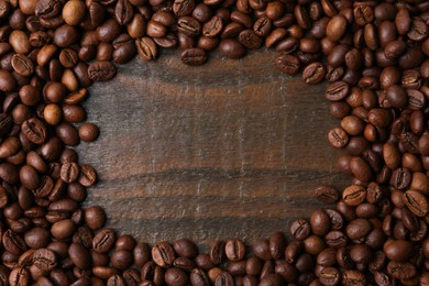 Photo of Frame of aromatic coffee beans on wooden table, top view. Space for text