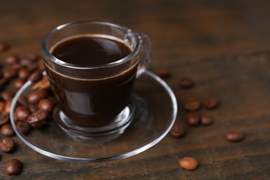 Photo of Aromatic coffee in glass cup and beans on wooden table, closeup. Space for text