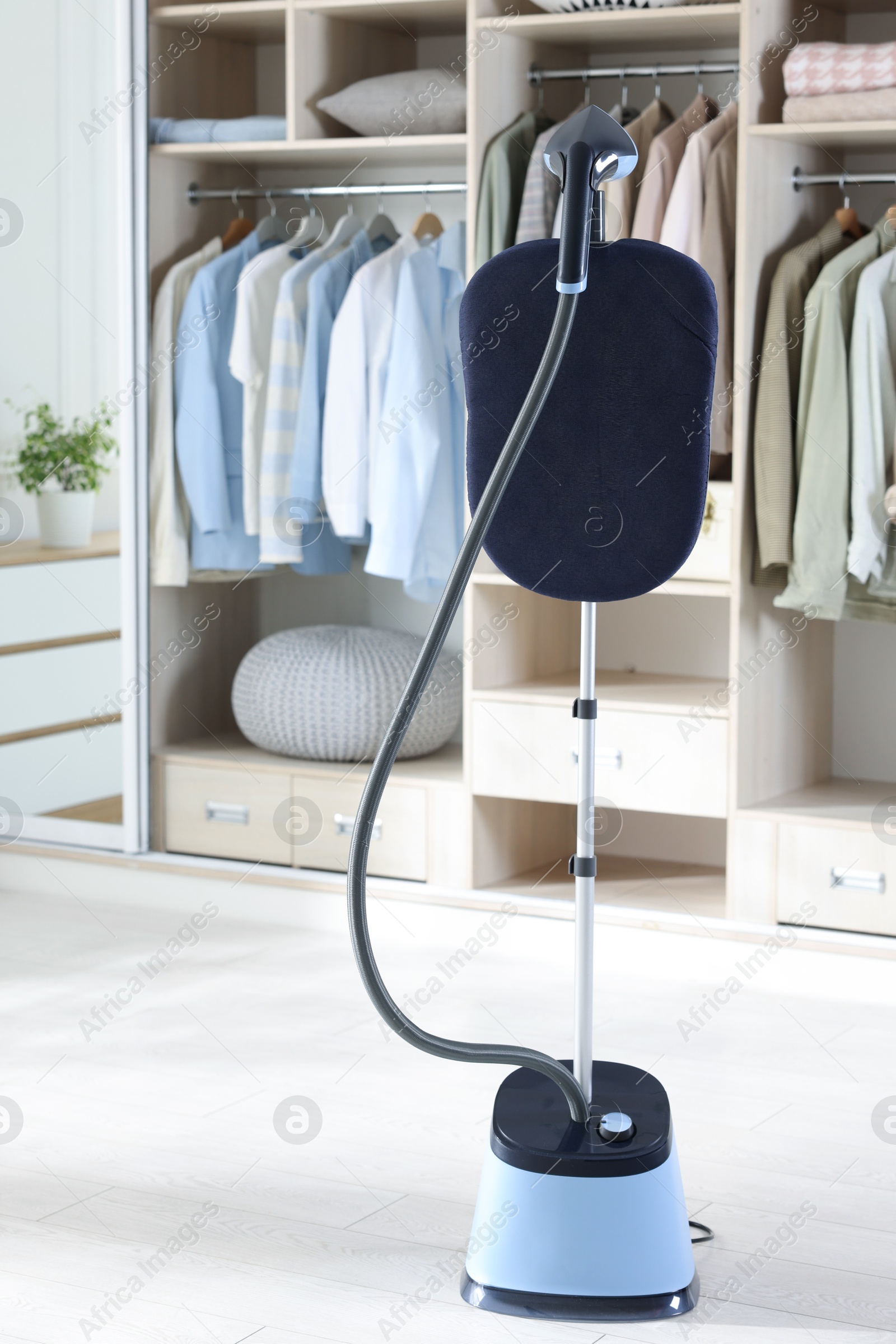 Modern upright steamer with stand and wardrobe indoors Photo of Modern upright steamer with stand and wardrobe indoors