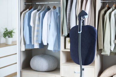 Photo of Modern upright steamer with stand near wardrobe indoors
