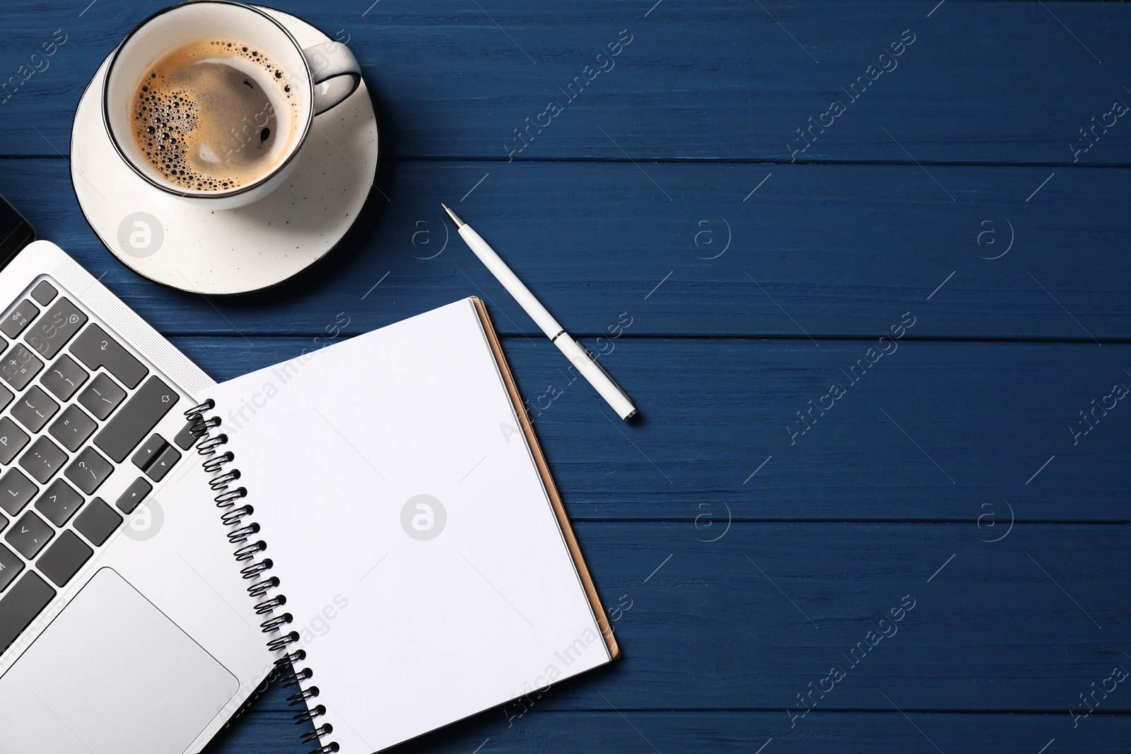Photo of Notebook with pen, laptop and coffee on blue wooden table, flat lay. Space for text