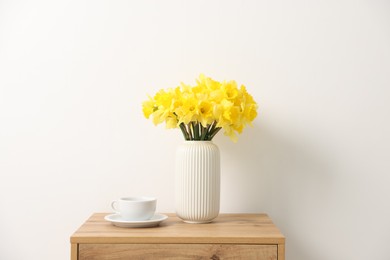 Photo of Beautiful daffodils in vase on wooden bedside table at home