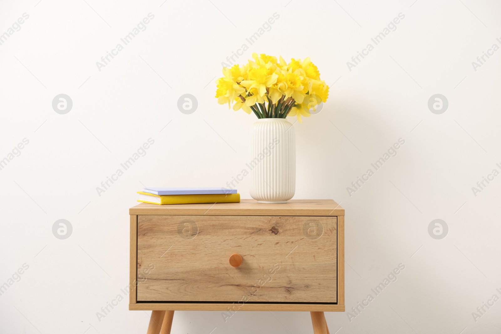 Beautiful daffodils in vase on wooden bedside table at home Photo of Beautiful daffodils in vase on wooden bedside table at home