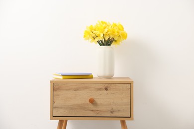 Photo of Beautiful daffodils in vase on wooden bedside table at home