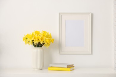 Photo of Beautiful daffodils in vase and books on white cabinet at home