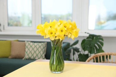 Photo of Beautiful daffodils in glass vase on table at home
