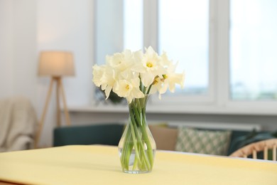 Photo of Beautiful daffodils in glass vase on table at home