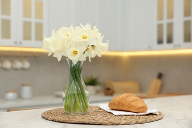 Photo of Beautiful daffodils in vase and croissant on white marble table indoors